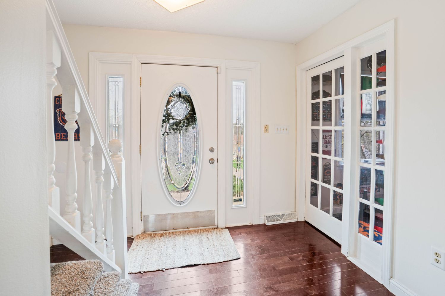 Bright foyer with hardwood floors, white front door with oval glass insert, sidelights, and French doors leading to an adjacent room.