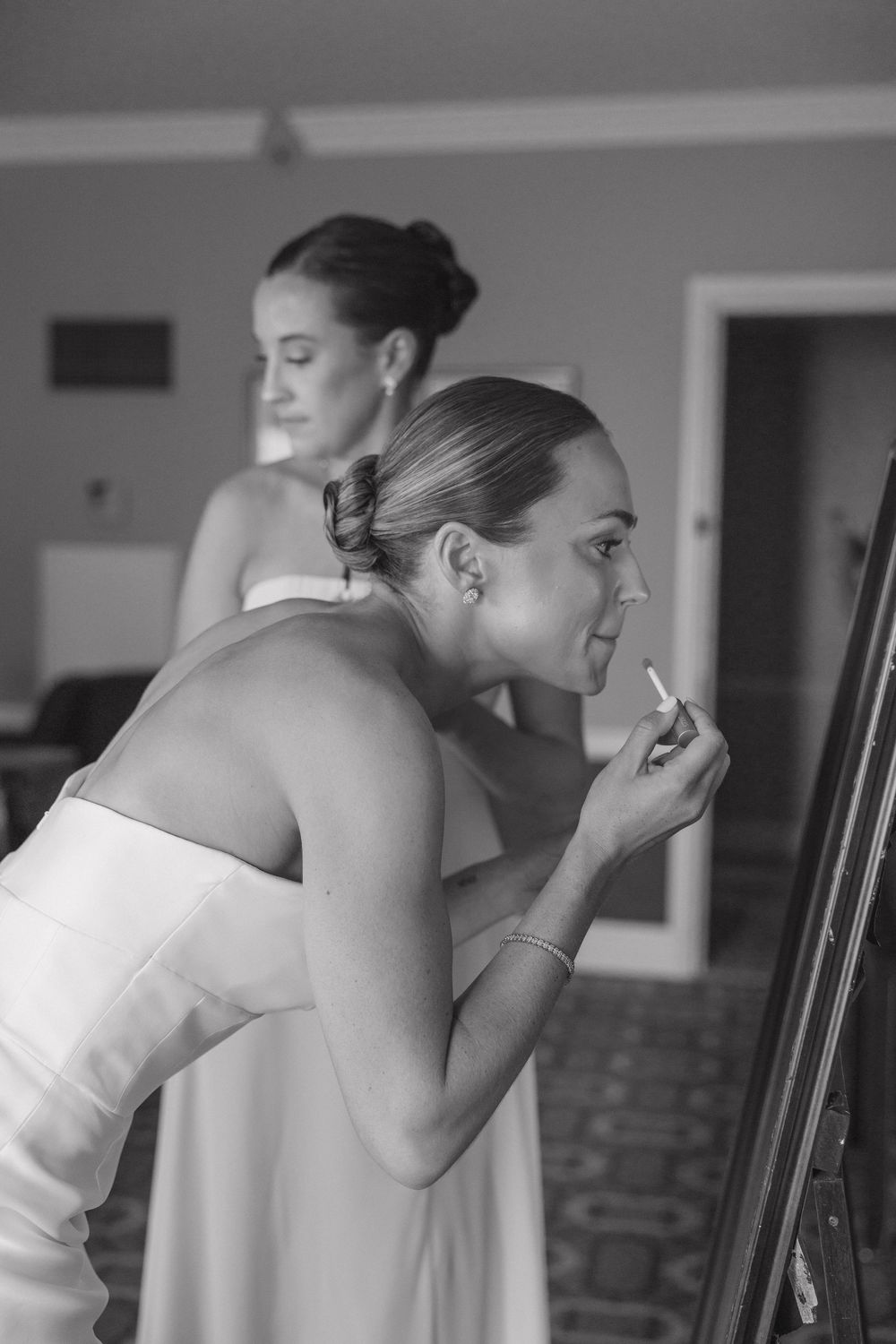 Black and white series showing a bride getting her makeup professionally applied while seated indoors.