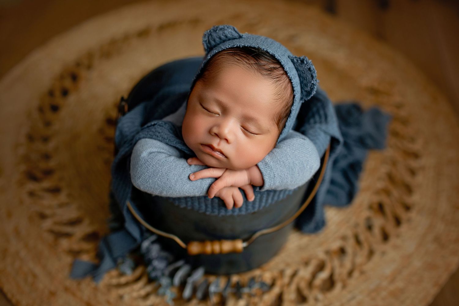 Newborn baby boy wearing blue onesie and bear hat bonnet posing in bucket at Flowertown Photography in Summerville, SC
