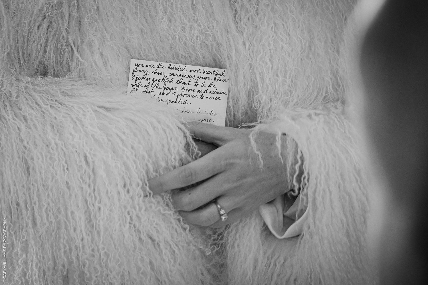 A hand holds the bride's vows against a white bridal jacket in a black and white photograph at Islington Town Hall.