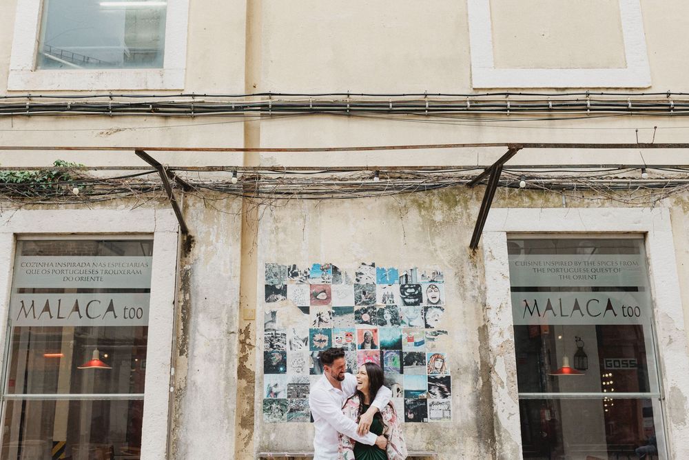 pre wedding photos in Lisbon LX Factory couple laughing in front of artistic collage wall