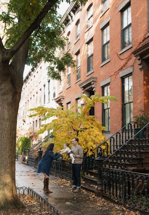 Autumn leaves scatter across the steps of a historic brownstone building in Brooklyn with iron railings and mature trees.