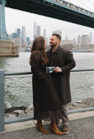 A couple shares a romantic moment by the waterfront with the city skyline visible in the background.