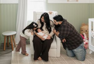 A family gathers around a newborn baby on a white couch in a cozy living room setting.