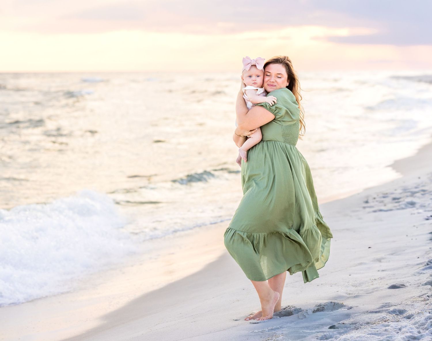 A person in a flowing sage green dress twirls joyfully along a sandy beach at sunset.