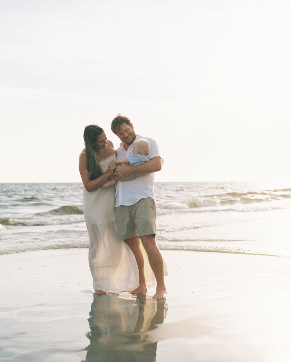 A couple embraces in shallow ocean water during sunset creating a romantic silhouette against the golden light.