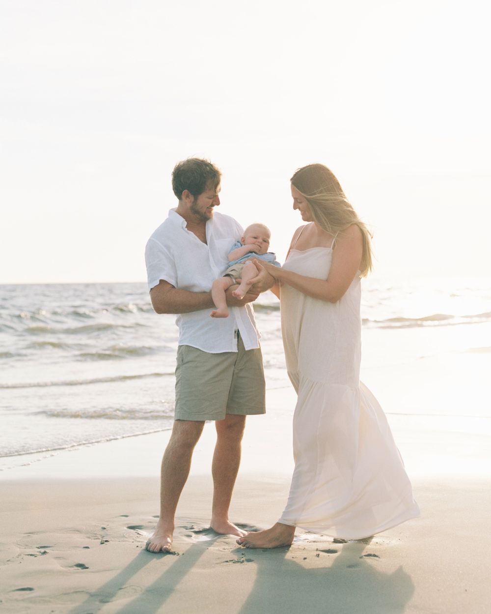 Couple shares romantic moments on a sunlit beach during a seaside proposal photoshoot.