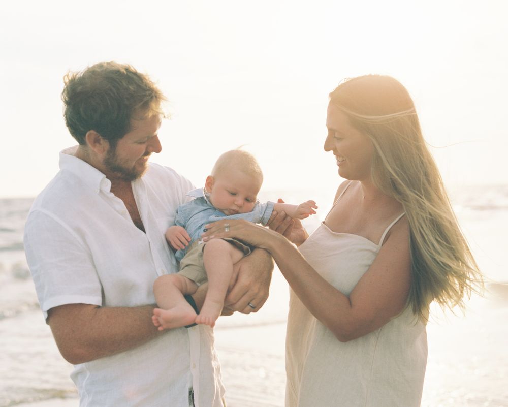 Family enjoying tender moments together on a sunlit beach during a photo session.