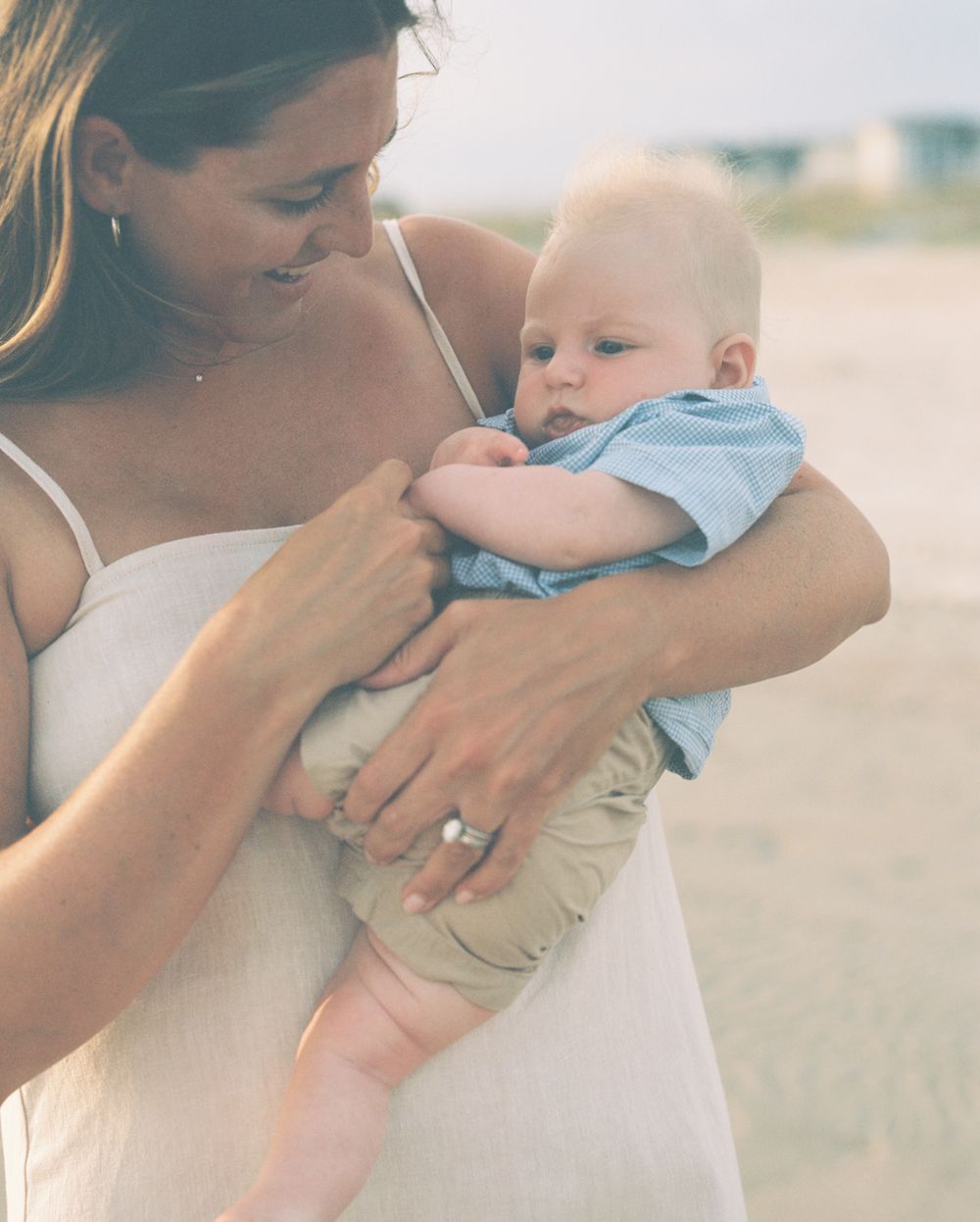 A tender moment between parent and baby on a sunny beach, captured in a series of intimate embraces.