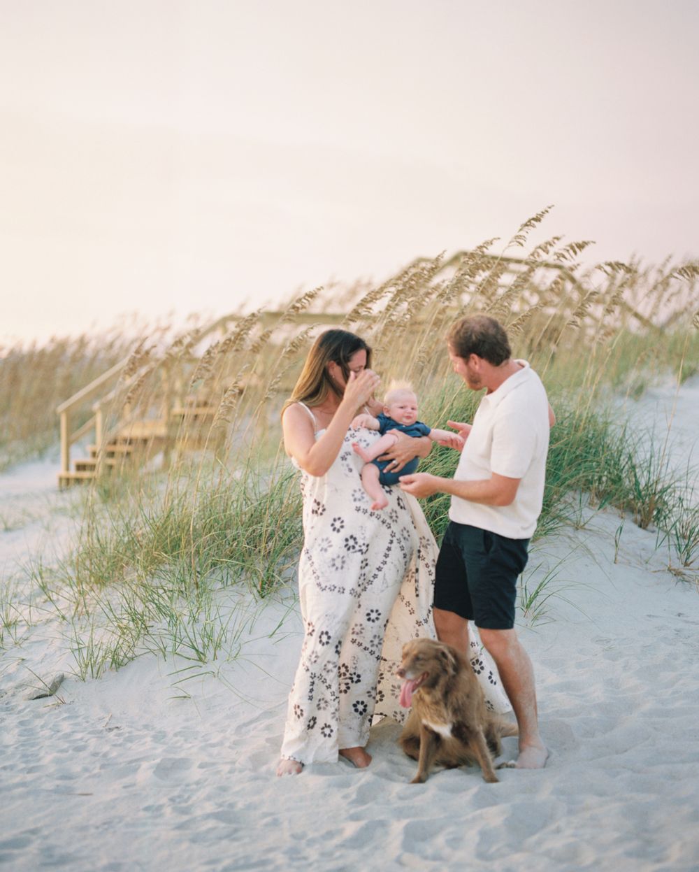 A couple plays with their dog among the sea oats on a coastal beach dune.