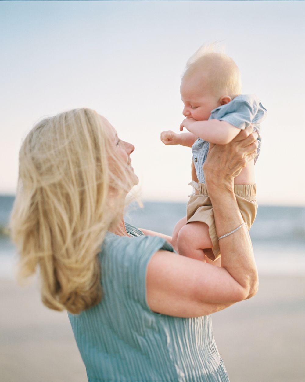 A tender moment between parent and baby on a sunny beach, with a series of joyful lifts and embraces.