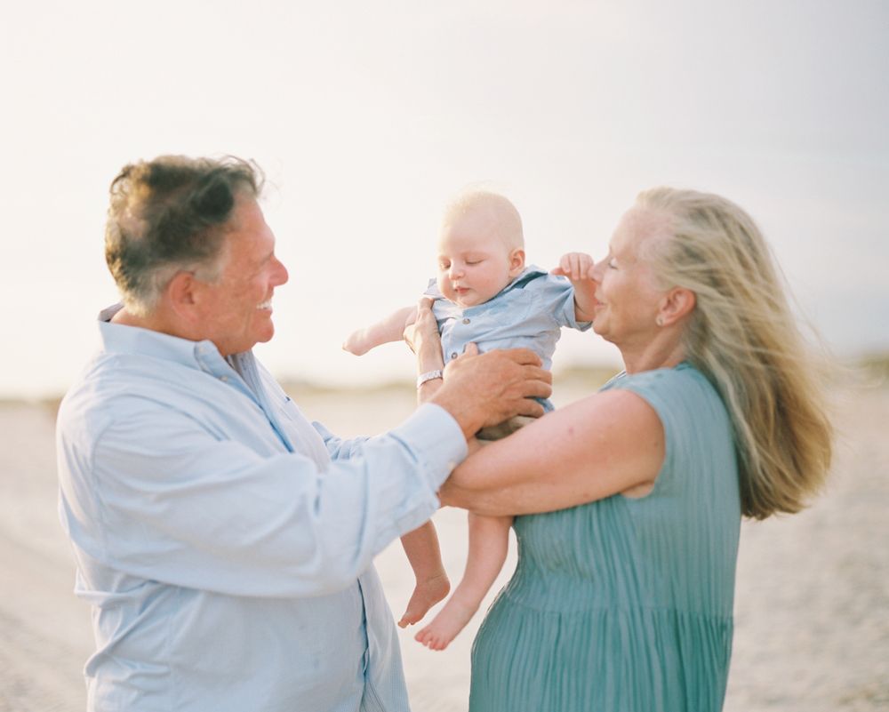A family shares playful moments together on a beach at sunset, lifting and holding their baby with love.