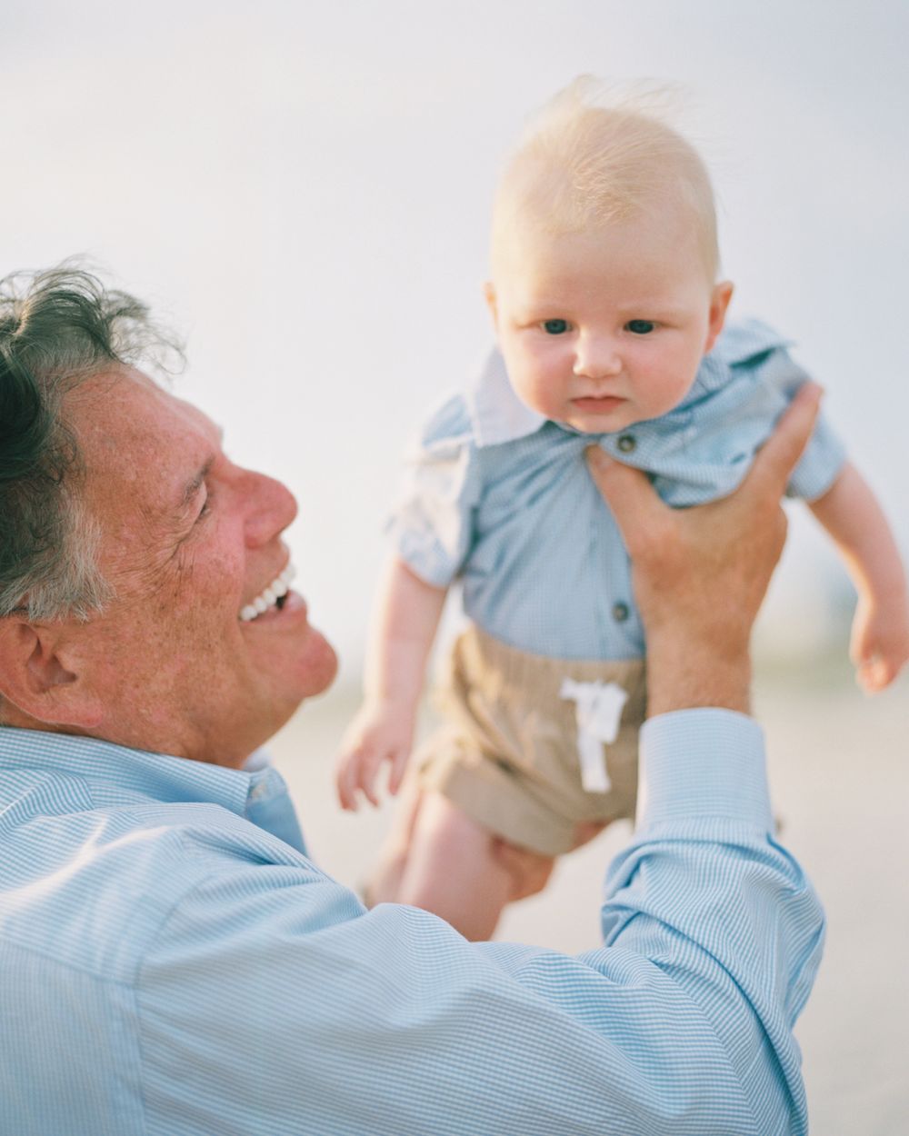 An endearing moment between an older person in blue and a baby wearing a light blue outfit on a bright day.