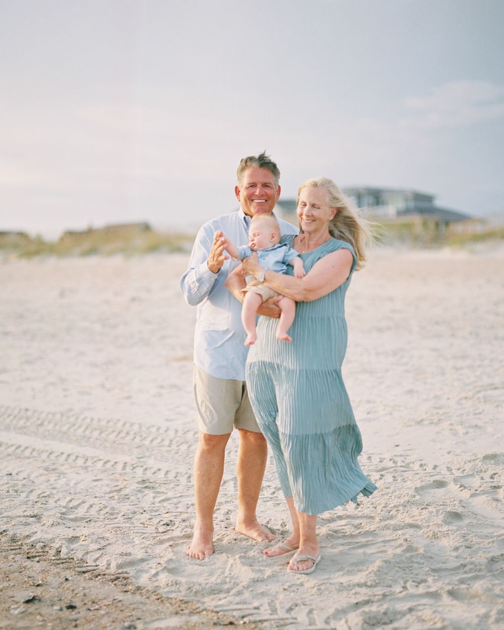 A family shares joyful moments together on a bright sandy beach wearing light blue and white outfits.