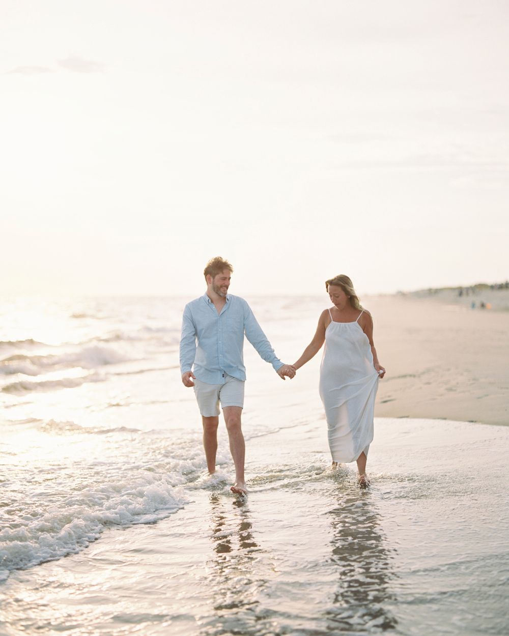 A couple holding hands while walking along the shoreline at sunset, their feet splashing in the gentle waves.