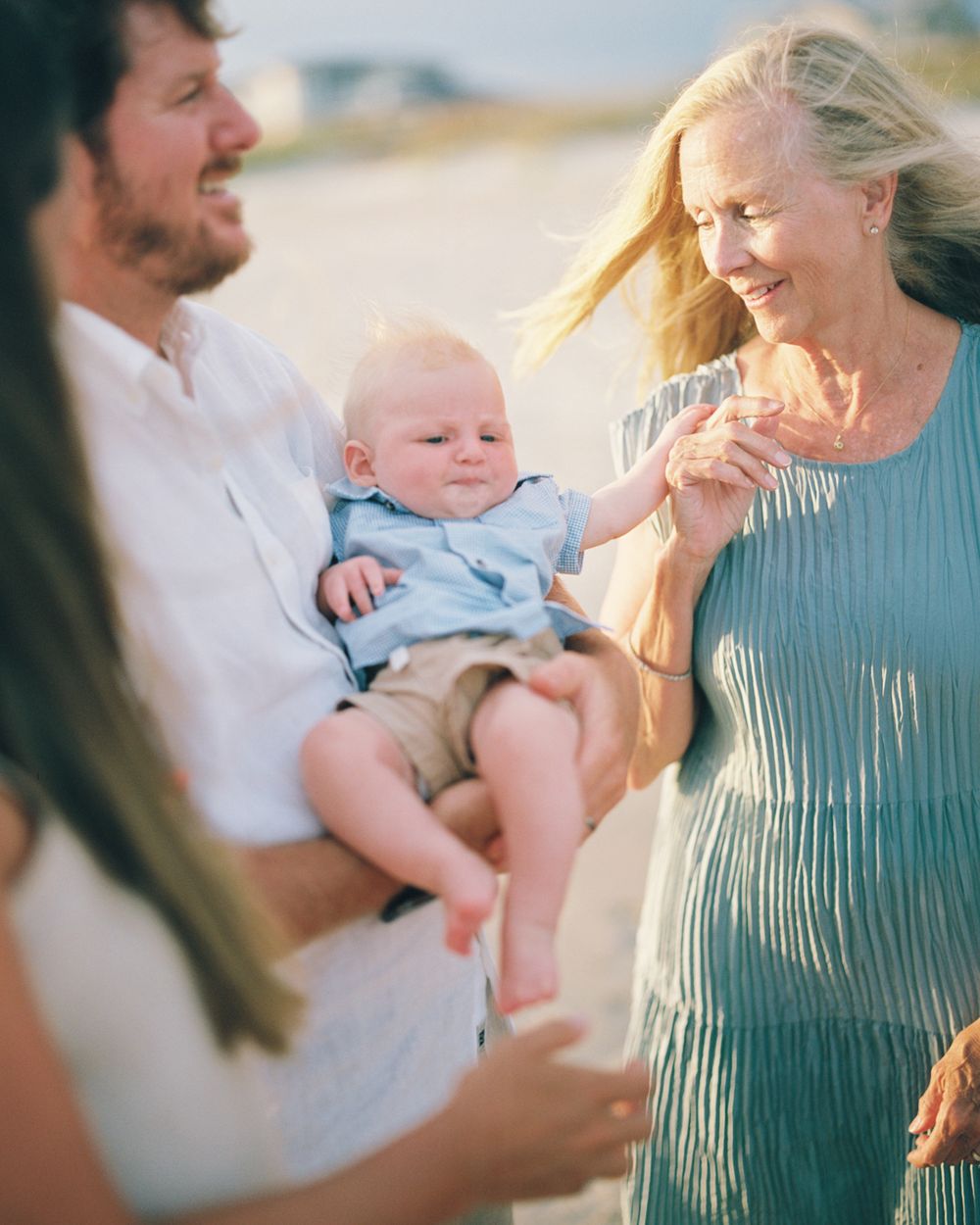 A group shares joyful moments with a baby on a beach during golden hour.