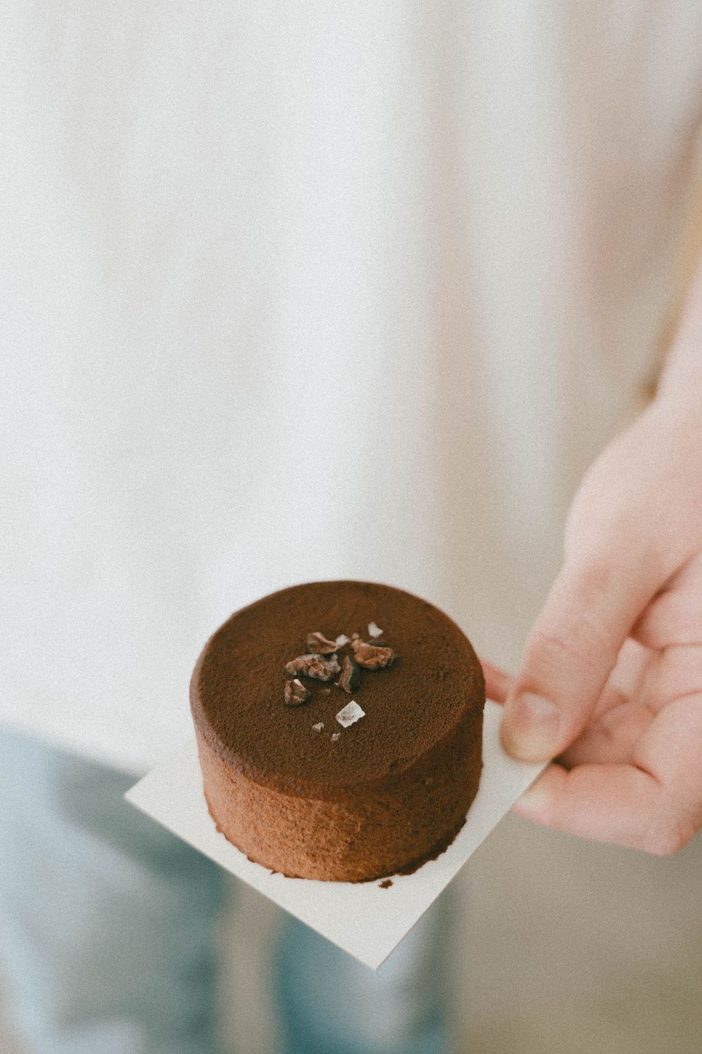 Main tenant un petit gâteau au chocolat rond saupoudré de poudre de cacao et garni de cacao, photo prise par la meilleure photographe du var