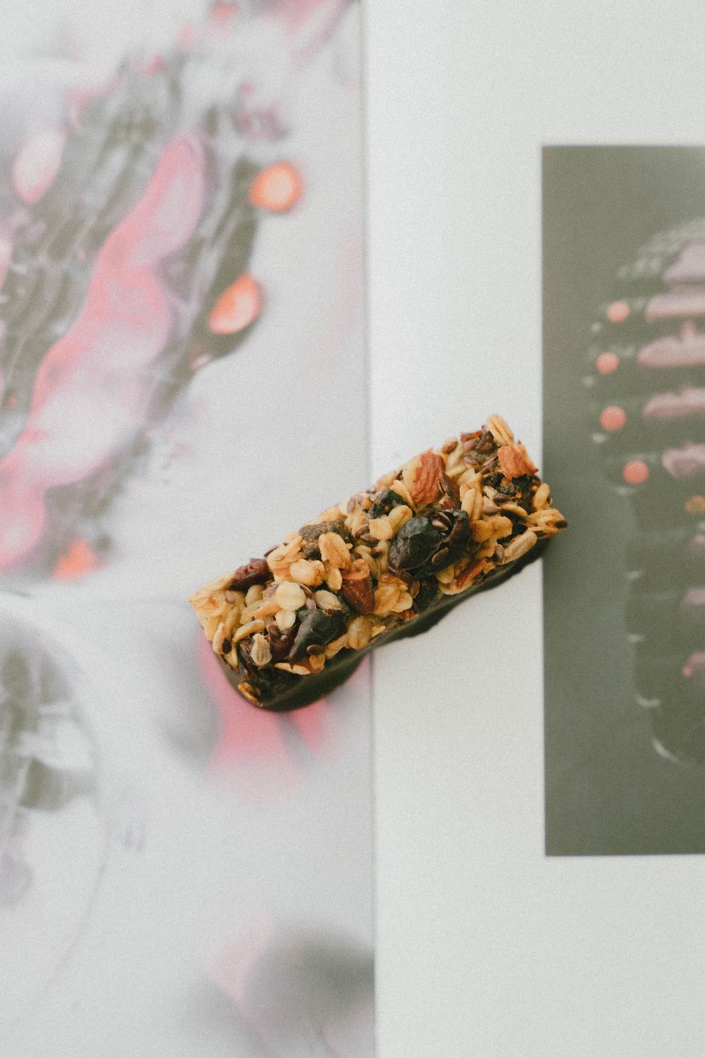 Une barre granola avec des noix et des graines reposant sur une page de magazine ouverte avec des illustrations florales.