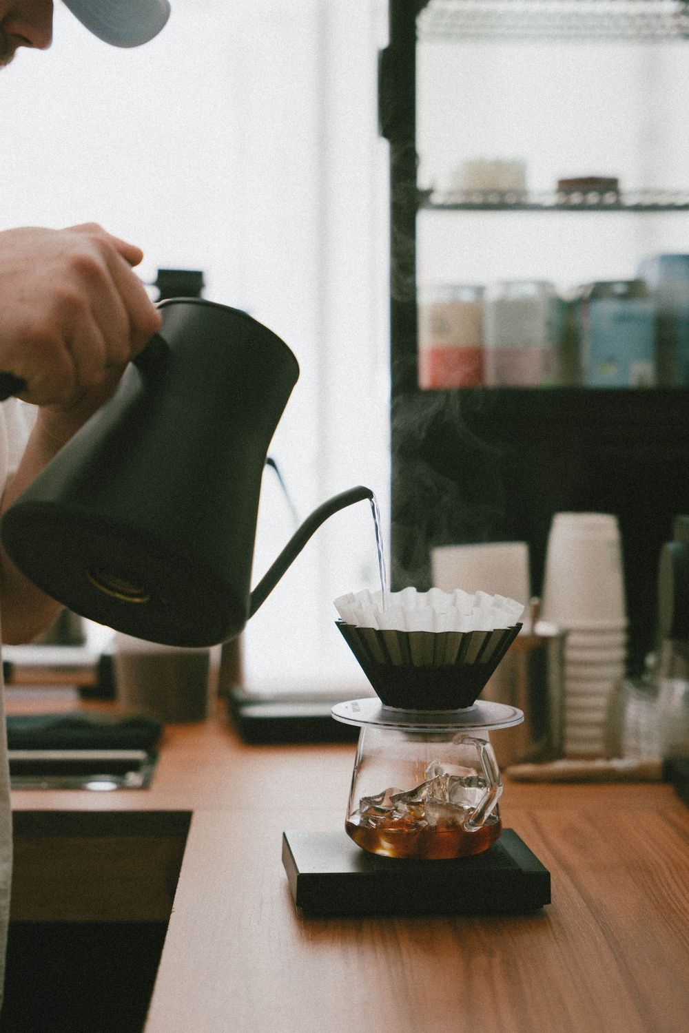 Barista versant de l'eau chaude d'une bouilloire à col de cygne dans un compte-gouttes à café sur un comptoir en bois.