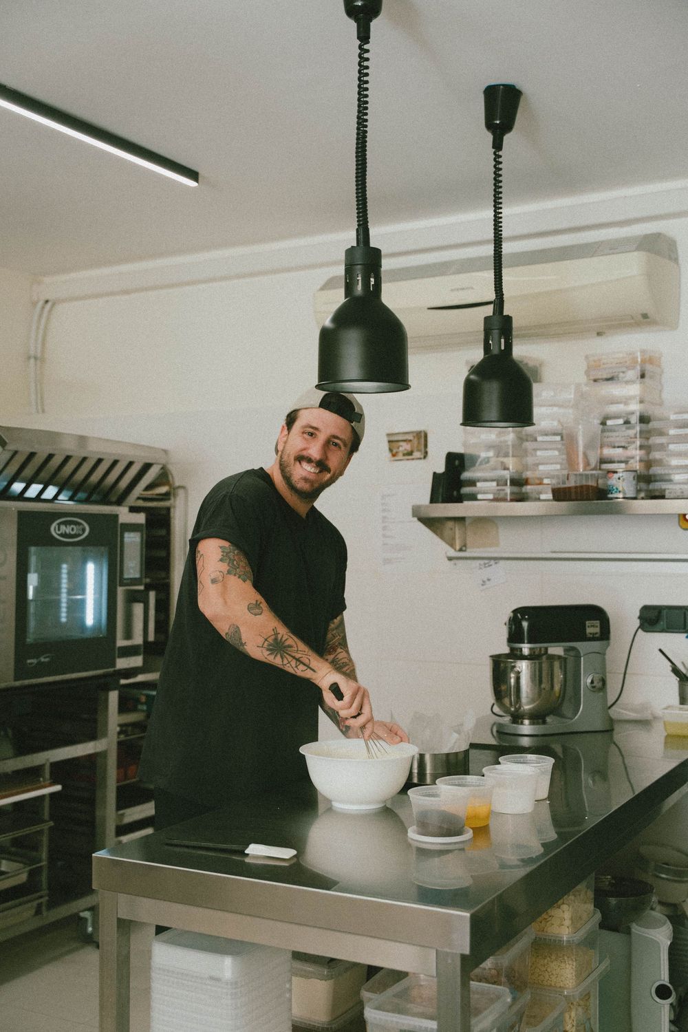 Chef masculin tatoué souriant tout en fouettant un bol sur un comptoir de cuisine en acier. photo prise par la meilleure photographe du var