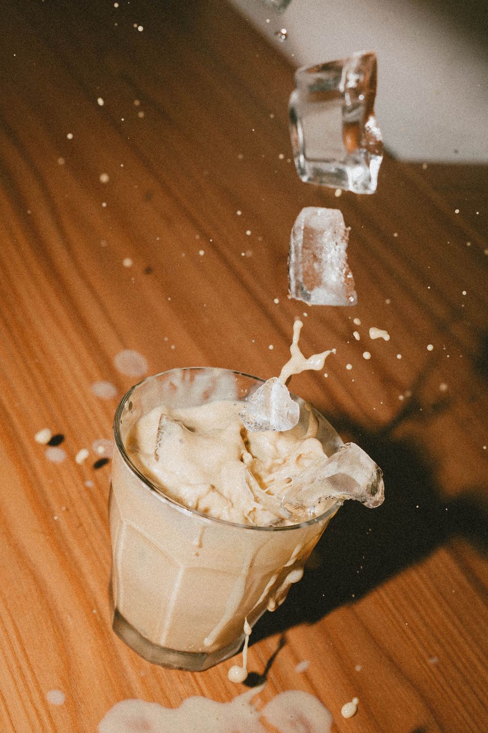 Des glaçons éclaboussant un verre de café glacé crémeux sur une table en bois, capturant le mouvement dynamique du liquide.