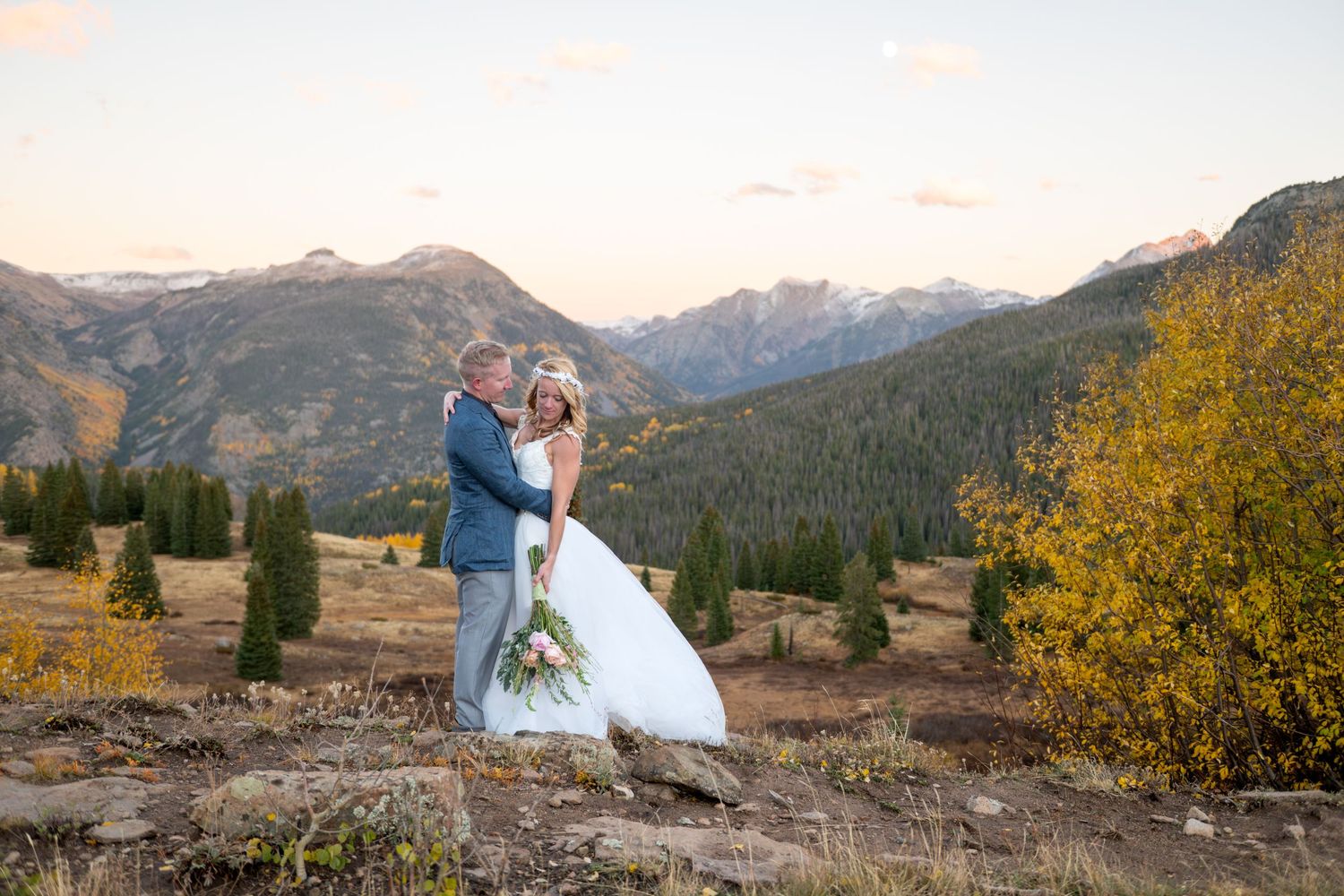 Bride and groom embrace on a mountain overlook with scenic San Juan Mountains  and autumn foliage at sunset.