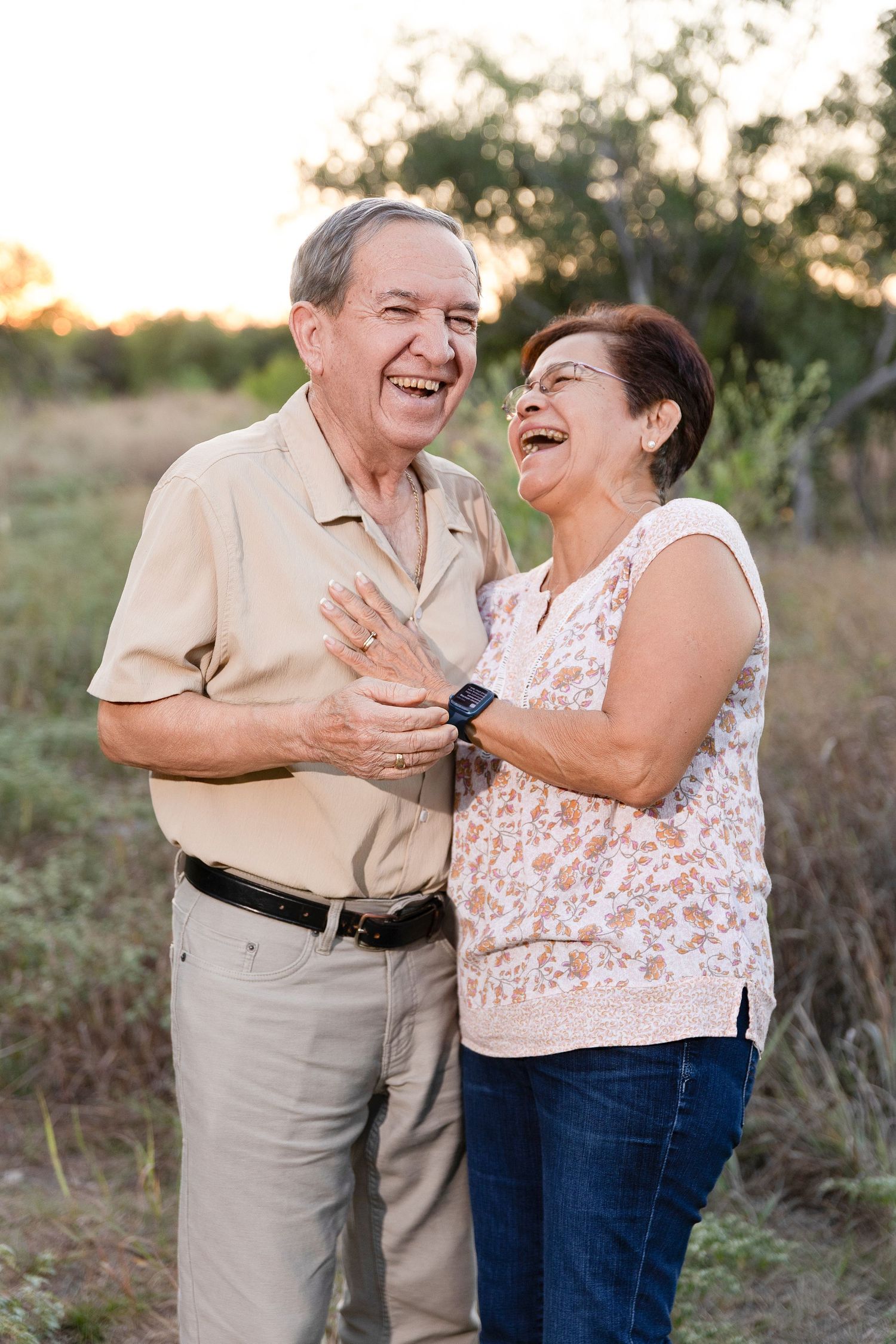 Elderly couple sharing a joyful laugh together outdoors during golden hour sunset.