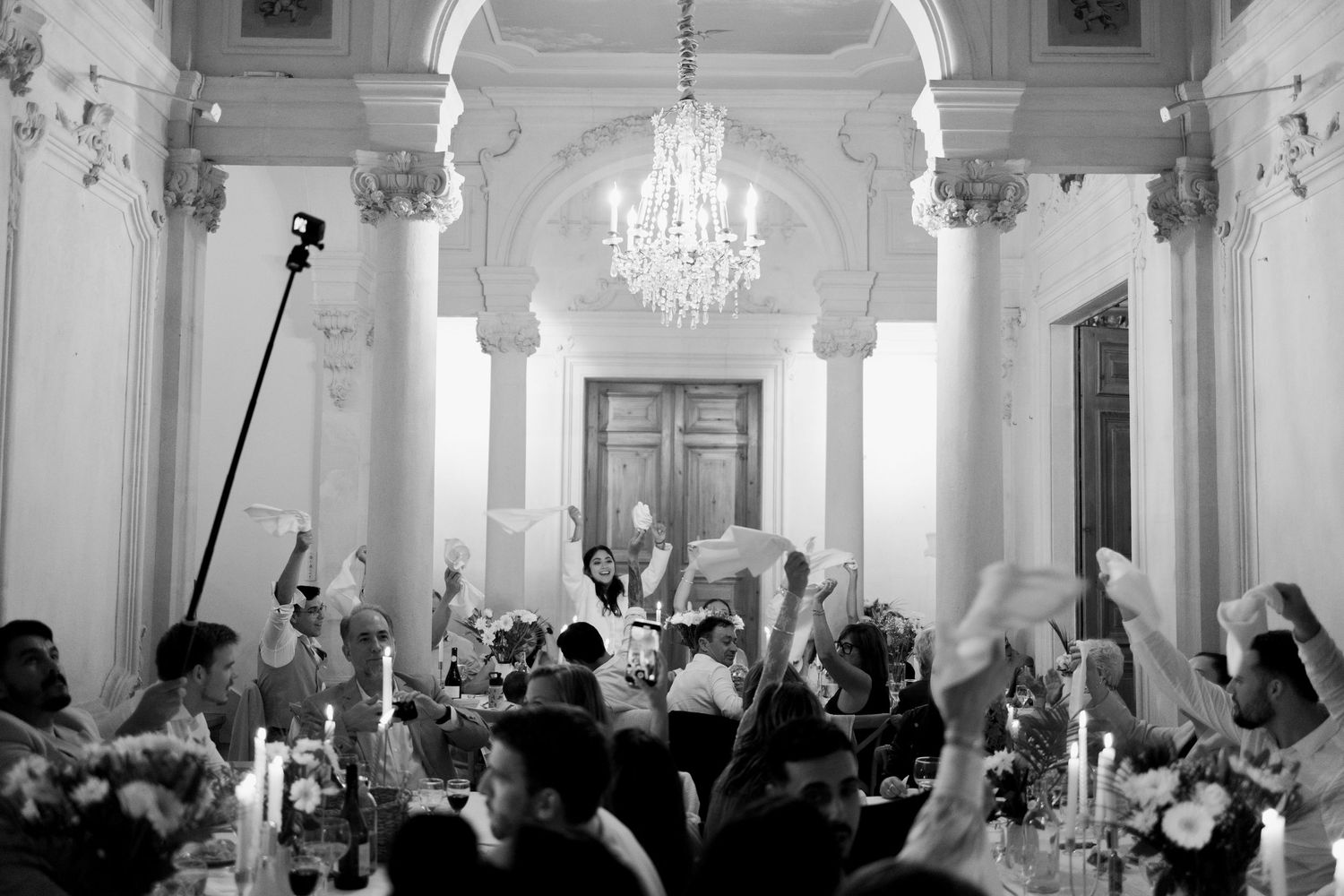 Family and friends cheer during reception and wave napkins in the air, celebrating the brides