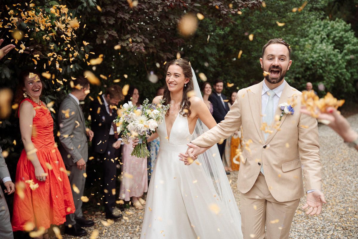 Wedding party celebrates with joyful confetti toss in outdoor garden setting.