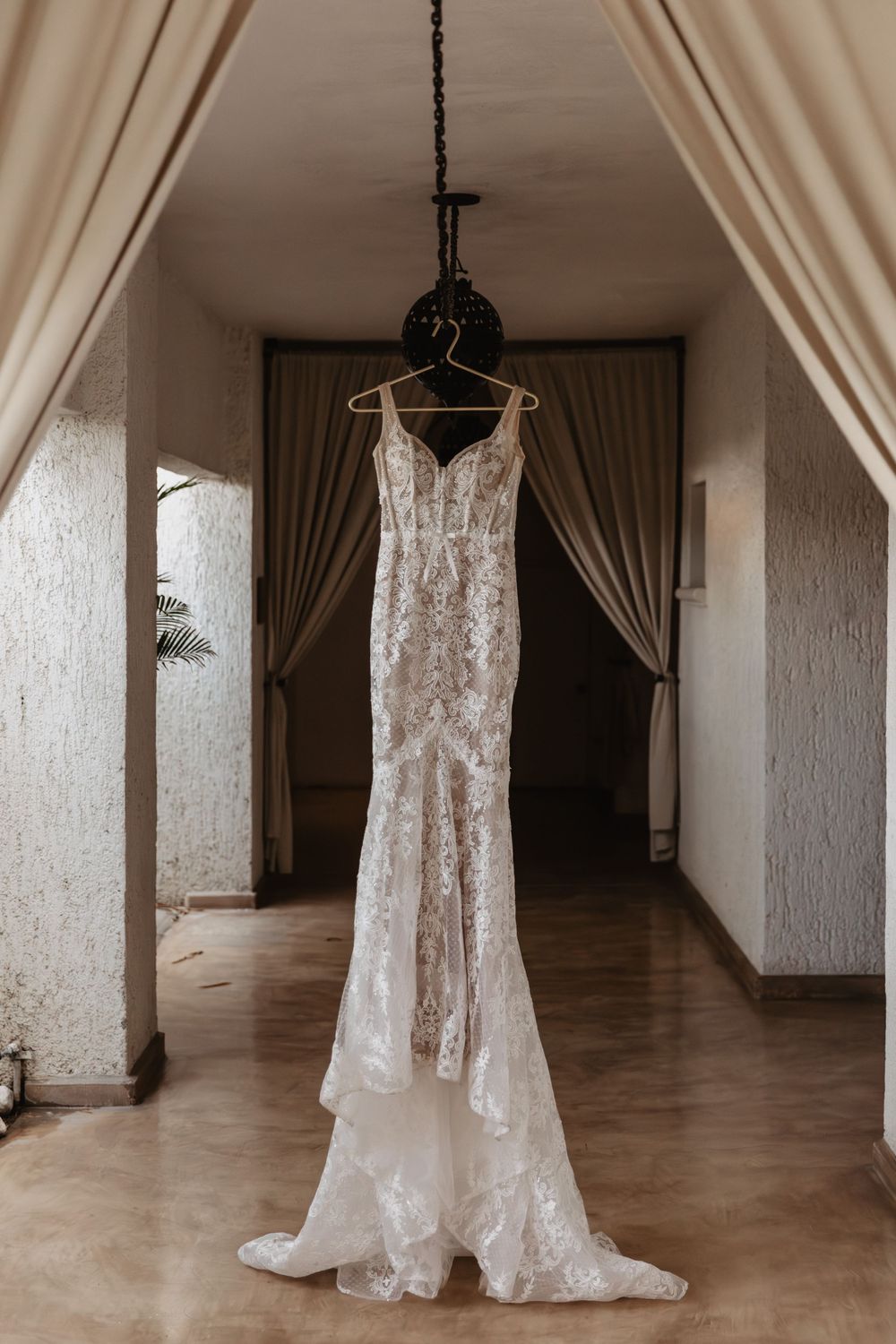 A collection of elegant white lace wedding dresses hanging from black hangers in a bright hallway with textured walls.