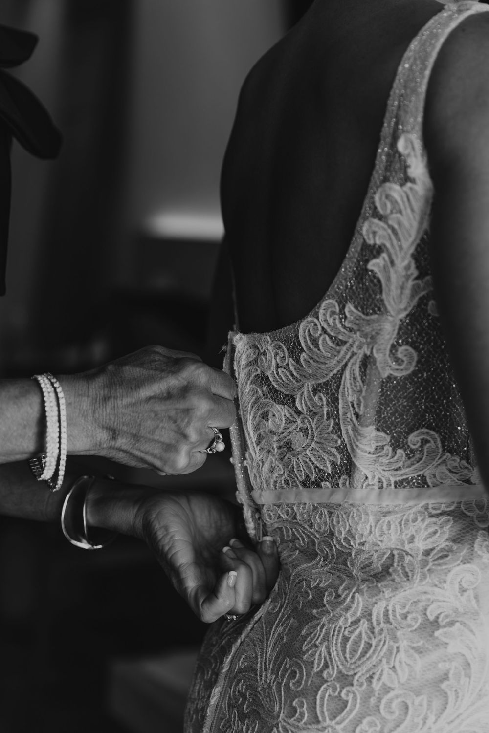 A series of black and white photos showing details of a delicate lace wedding dress being buttoned up.