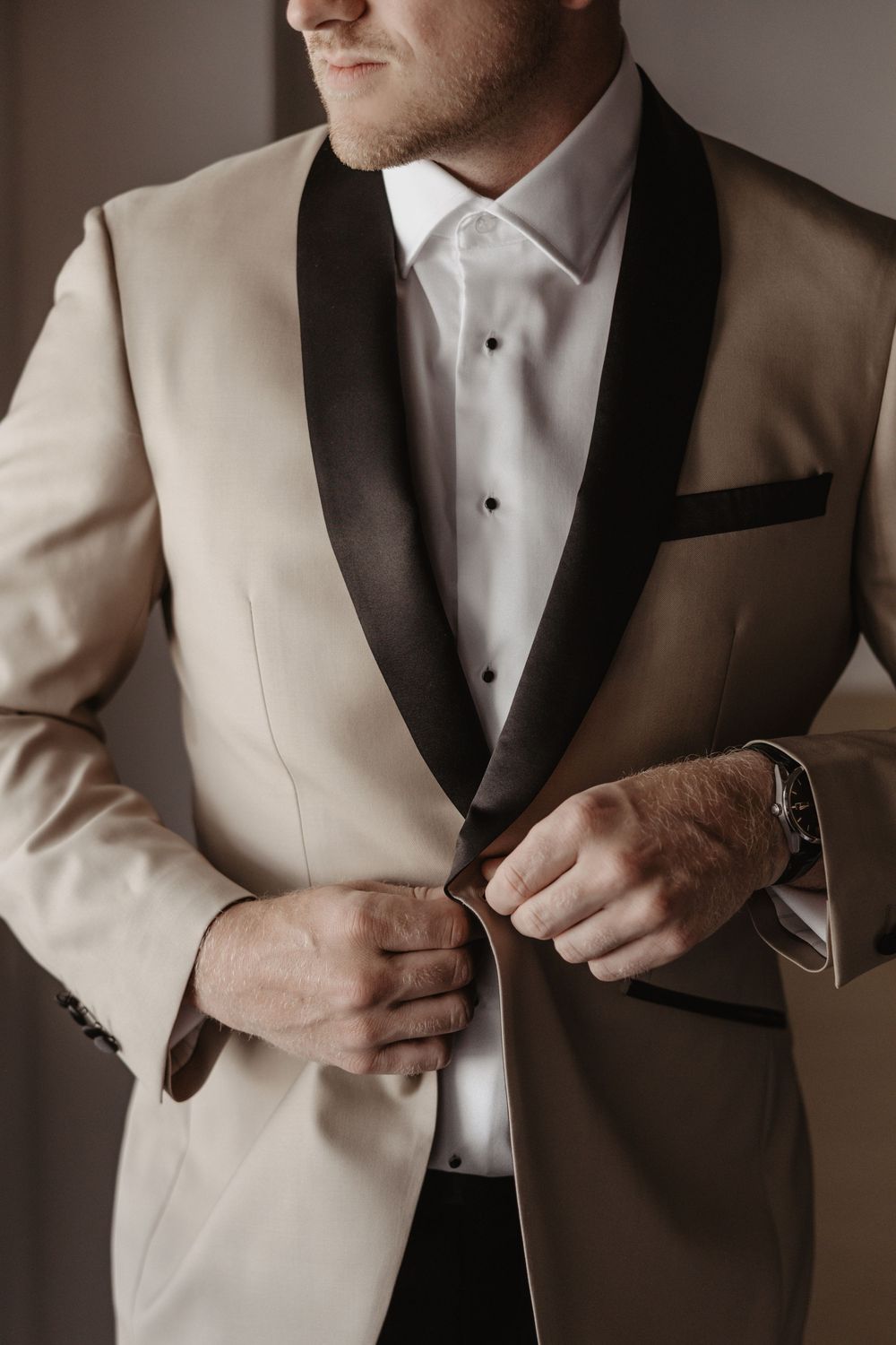 Close-up shot of hands adjusting a cream-colored tuxedo jacket with black lapels and white dress shirt.