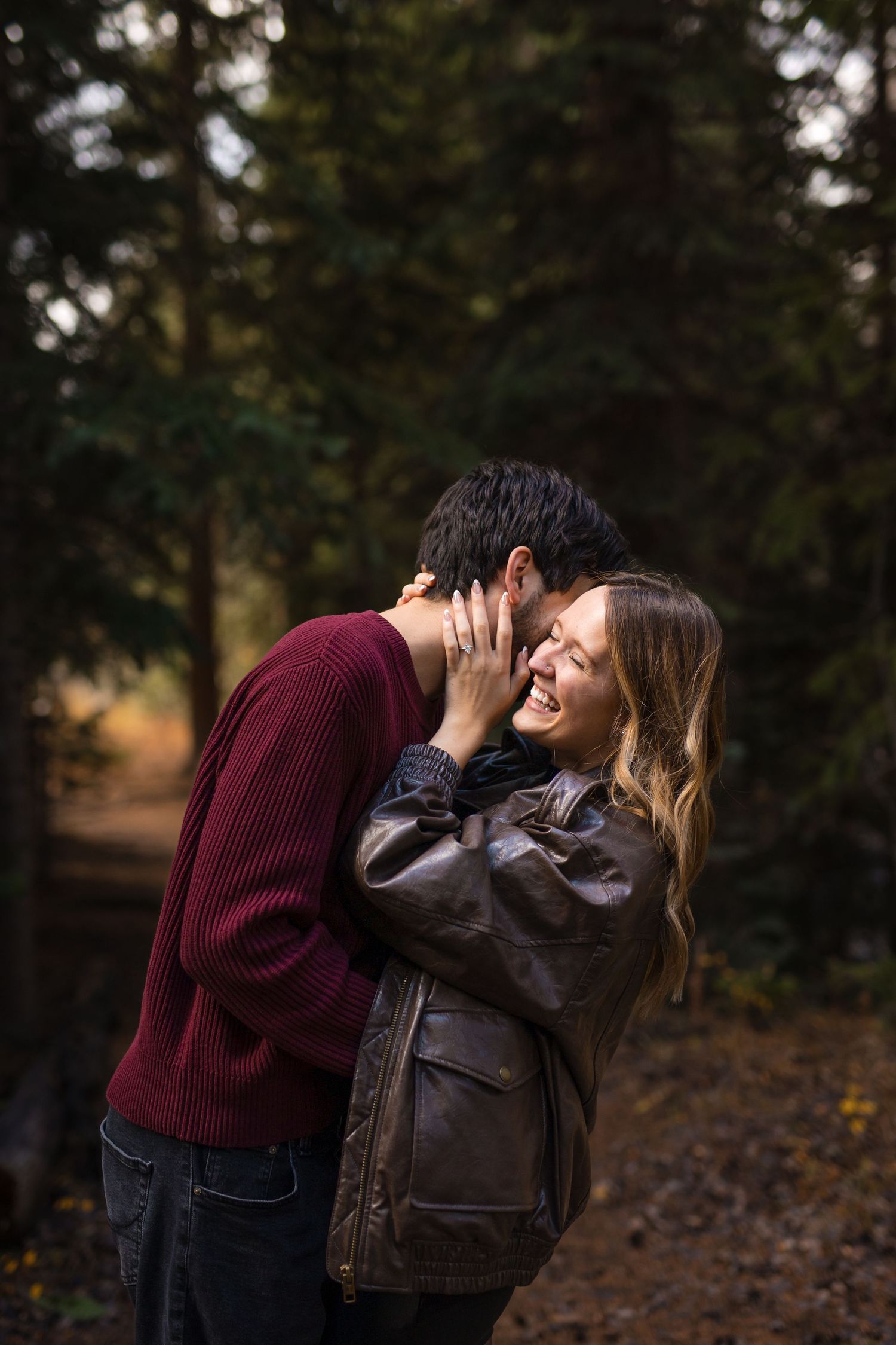 A couple in autumn attire sharing intimate moments outdoors in a wooded setting during golden hour.