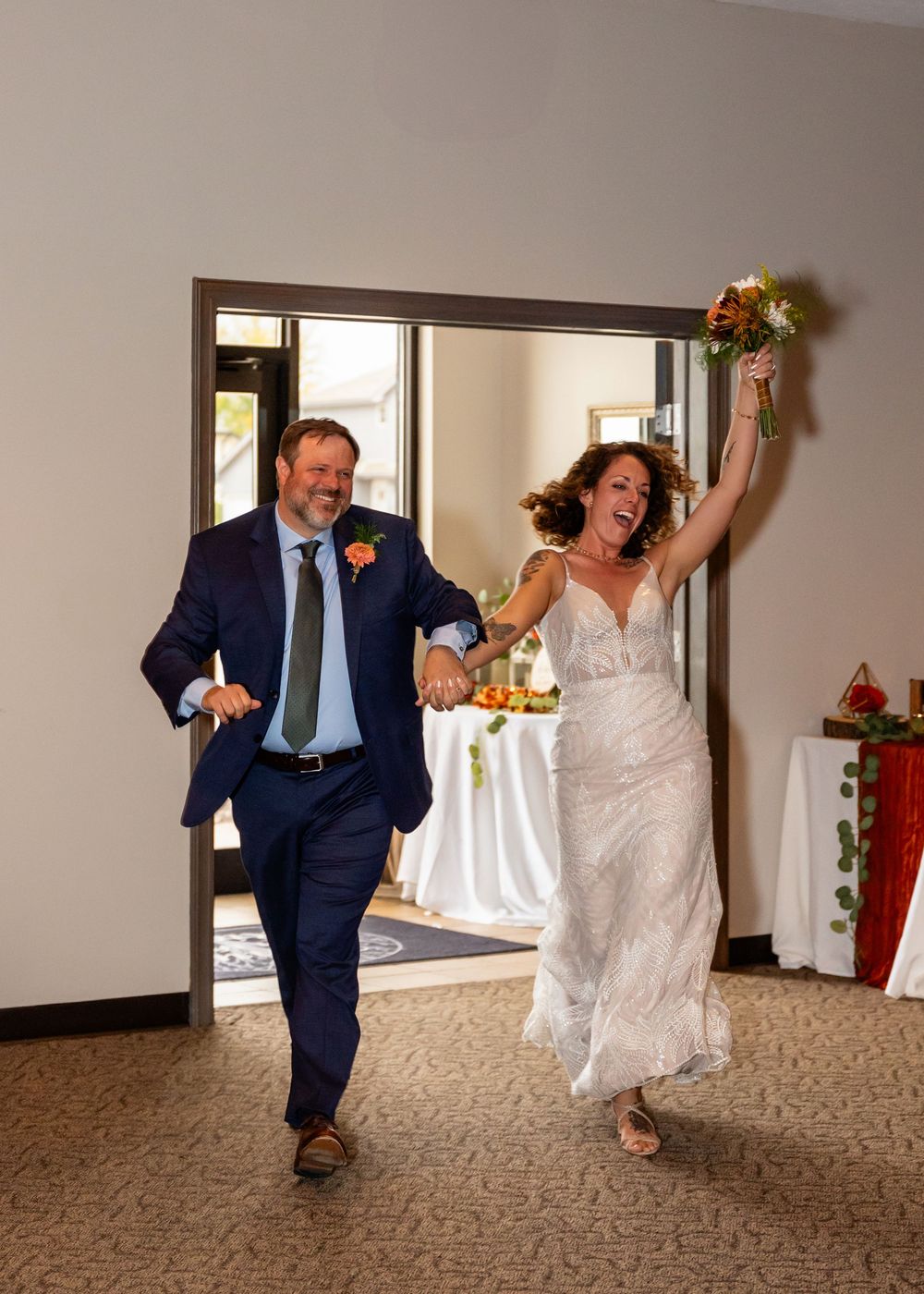 Joyful bride and groom make grand entrance at wedding reception, bride raising bouquet, groom in navy suit at a Venue on the Ridge  Elkhorn