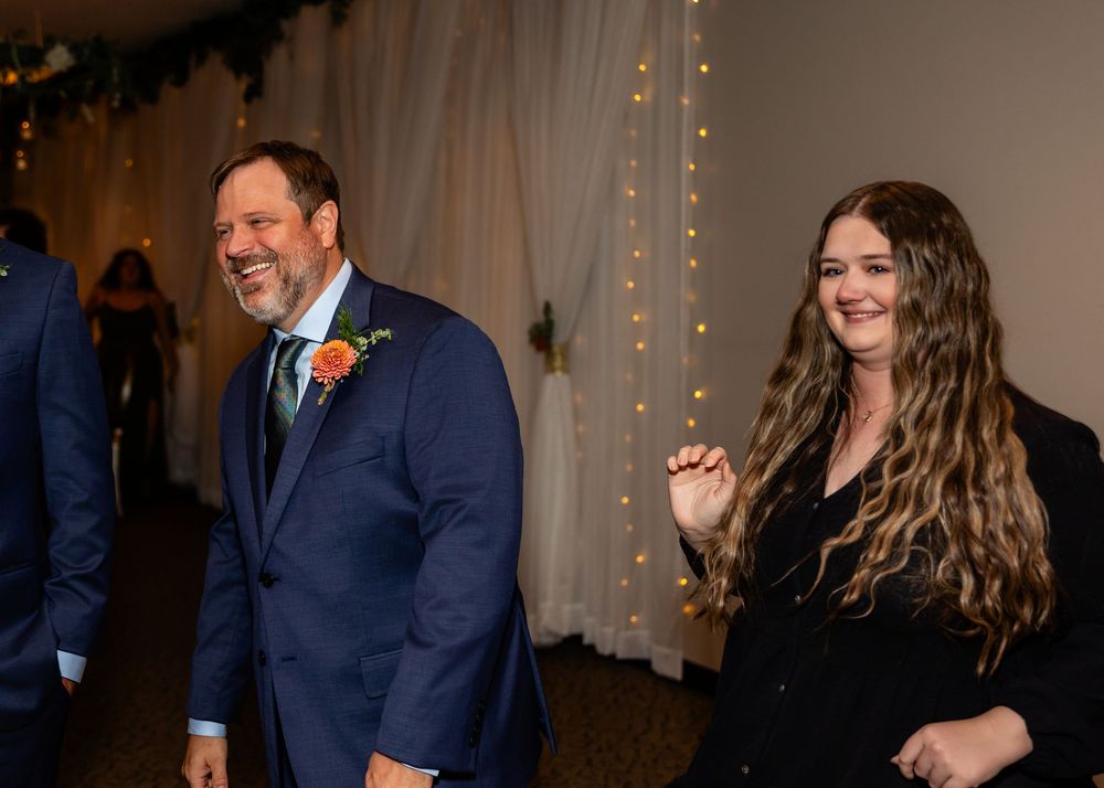 Man in blue suit with orange boutonniere and woman in black dress smiling at a wedding reception at a Venue on the Ridge in Elkhorn NE