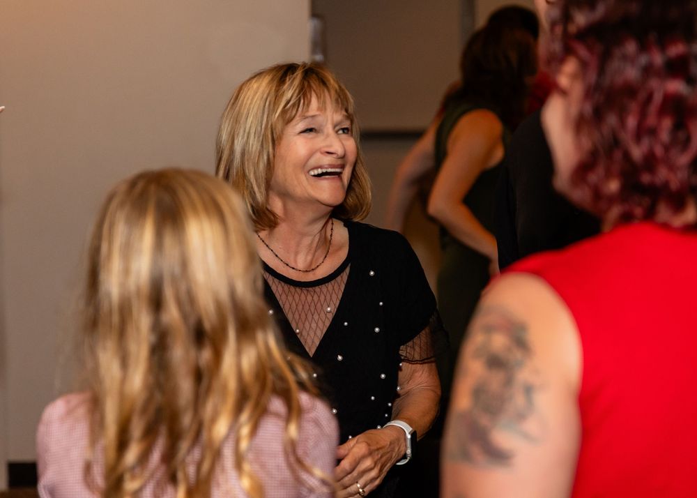 Woman in black top laughing joyfully while socializing at an indoor gathering with other guests at a Venue on the Ridge in Elkhorn NE