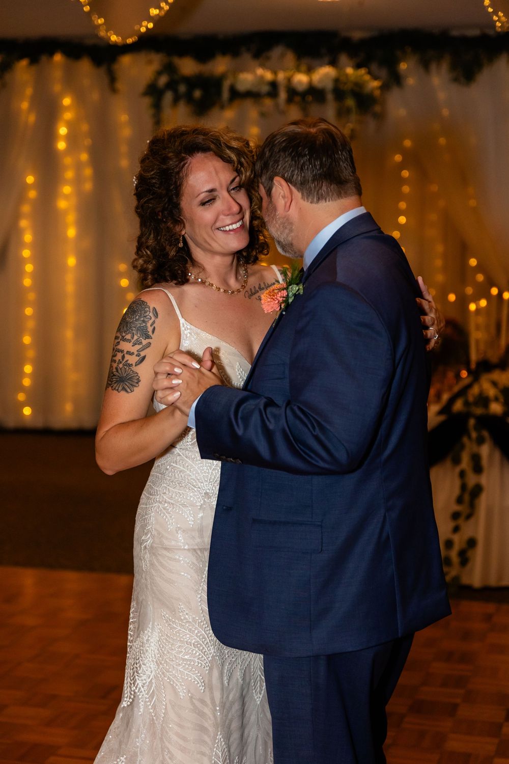 Bride and groom share their first dance, smiling joyfully, surrounded by warm fairy lights at their wedding reception.