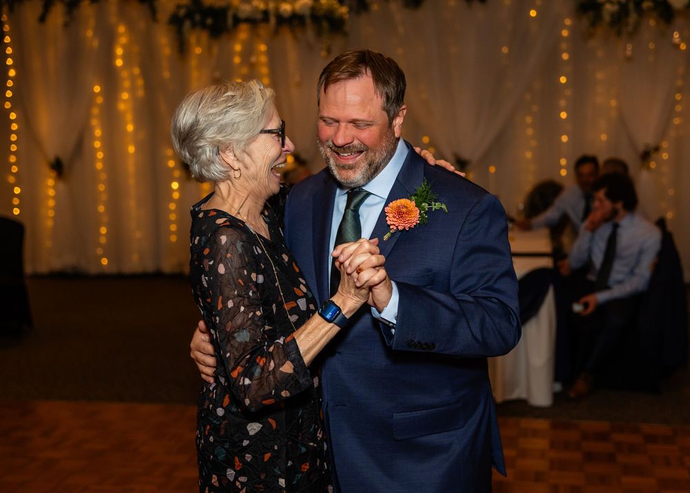 Elderly woman and suited man share a joyful mother-son dance at a warmly lit wedding reception at a Venue on the Ridge in Elkhorn NE