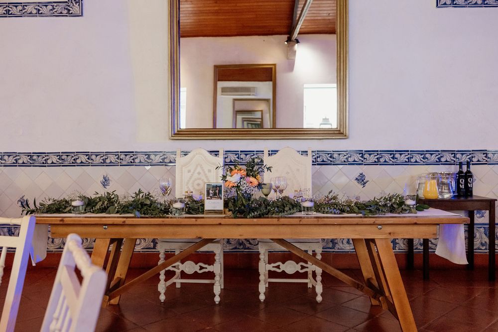 Rustic wooden dining table decorated with greenery centerpiece and candles in a Portuguese tiled room.