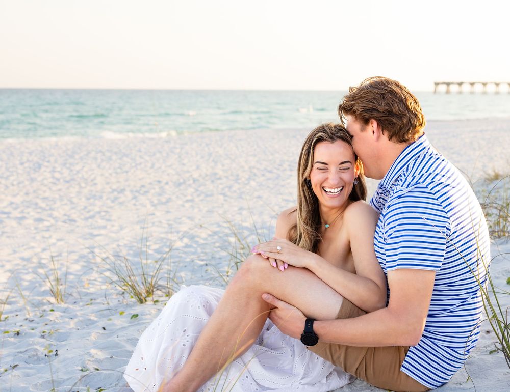 Happy couple sitting together on a white sandy beach, smiling and sharing a romantic moment by the ocean.