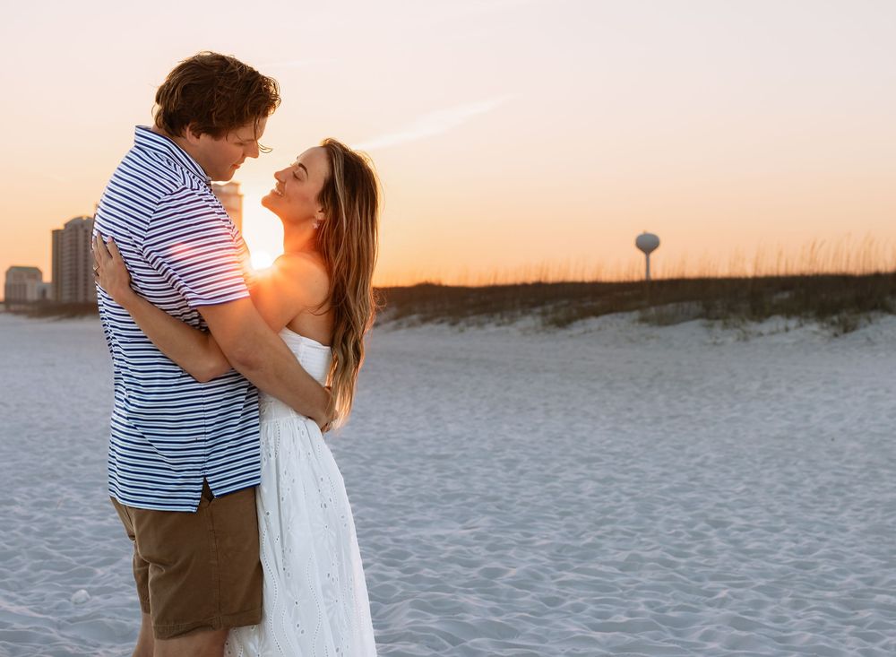 Romantic couple holding each other on sandy beach during golden sunset with dunes behind them.