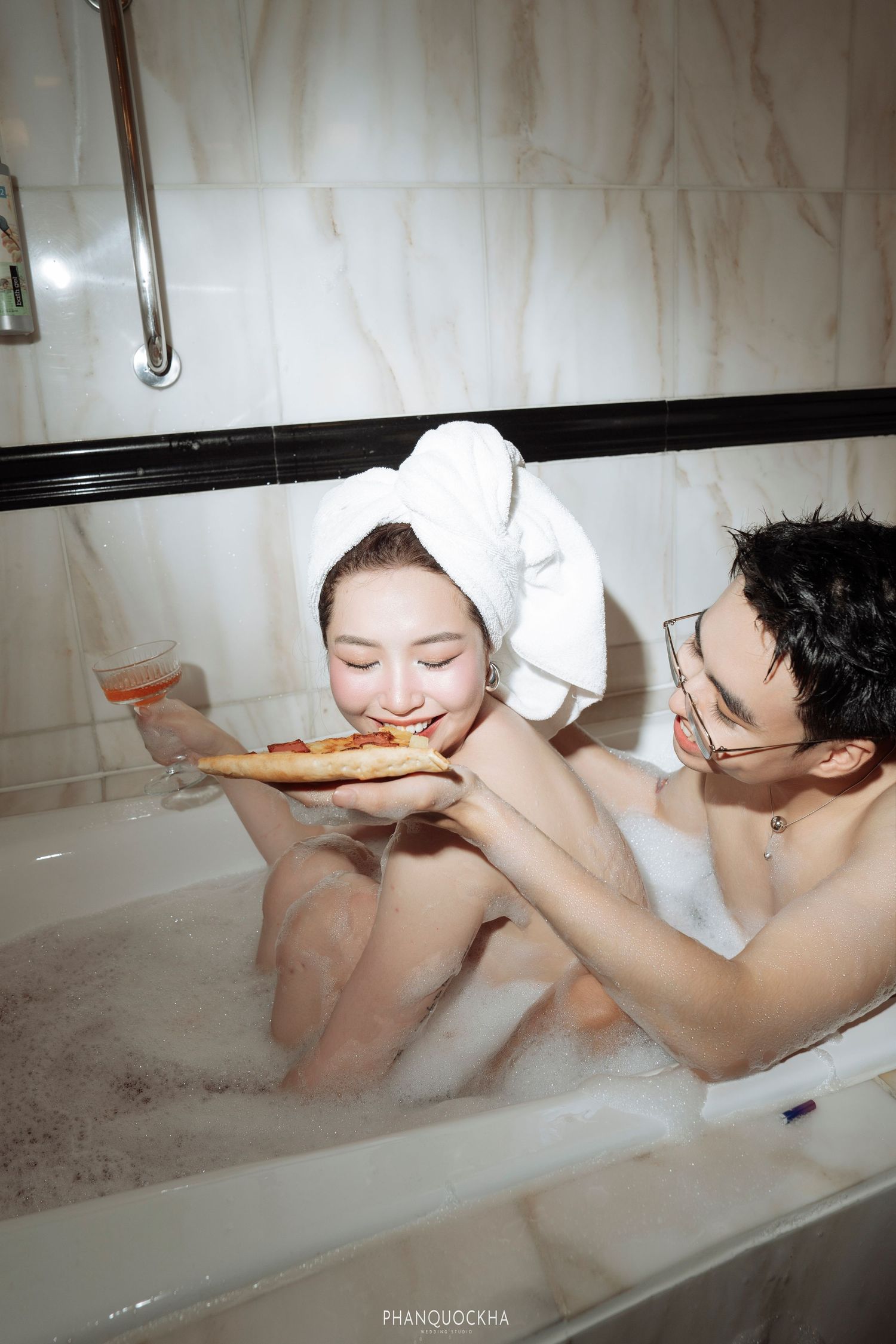 Playful couple shares pizza and wine while relaxing together in a bubble bath.