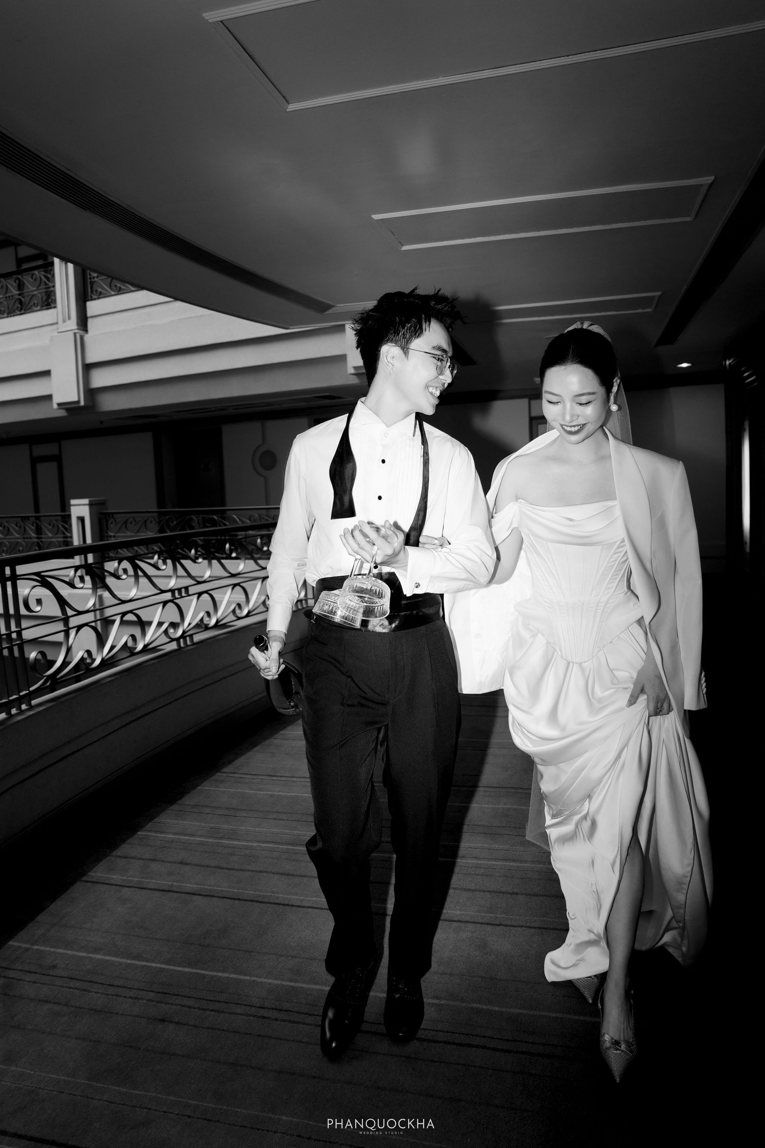 Black and white photo of elegant couple walking and laughing together along an indoor corridor.