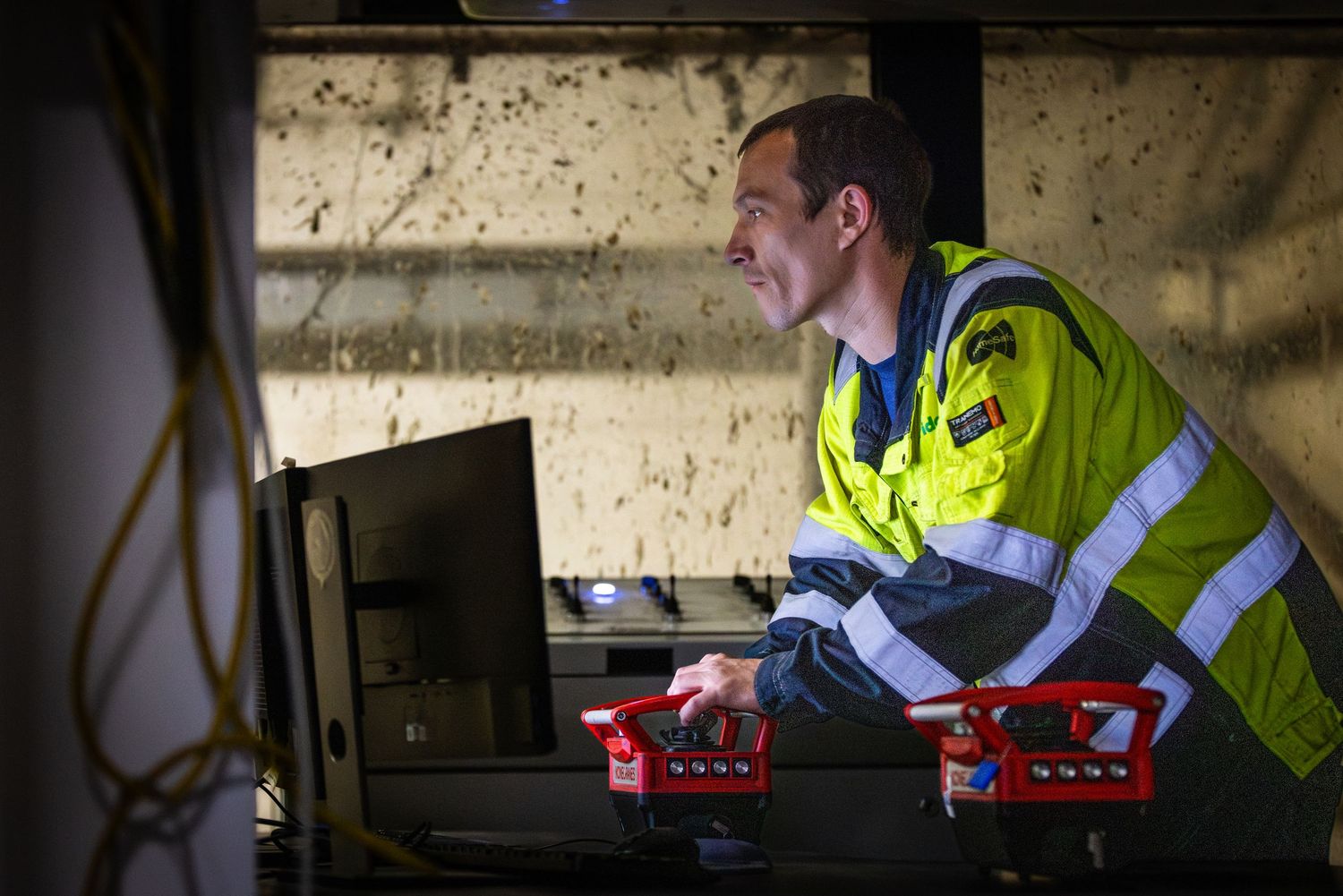 Worker in high-visibility safety vest operates equipment in dimly lit industrial setting.