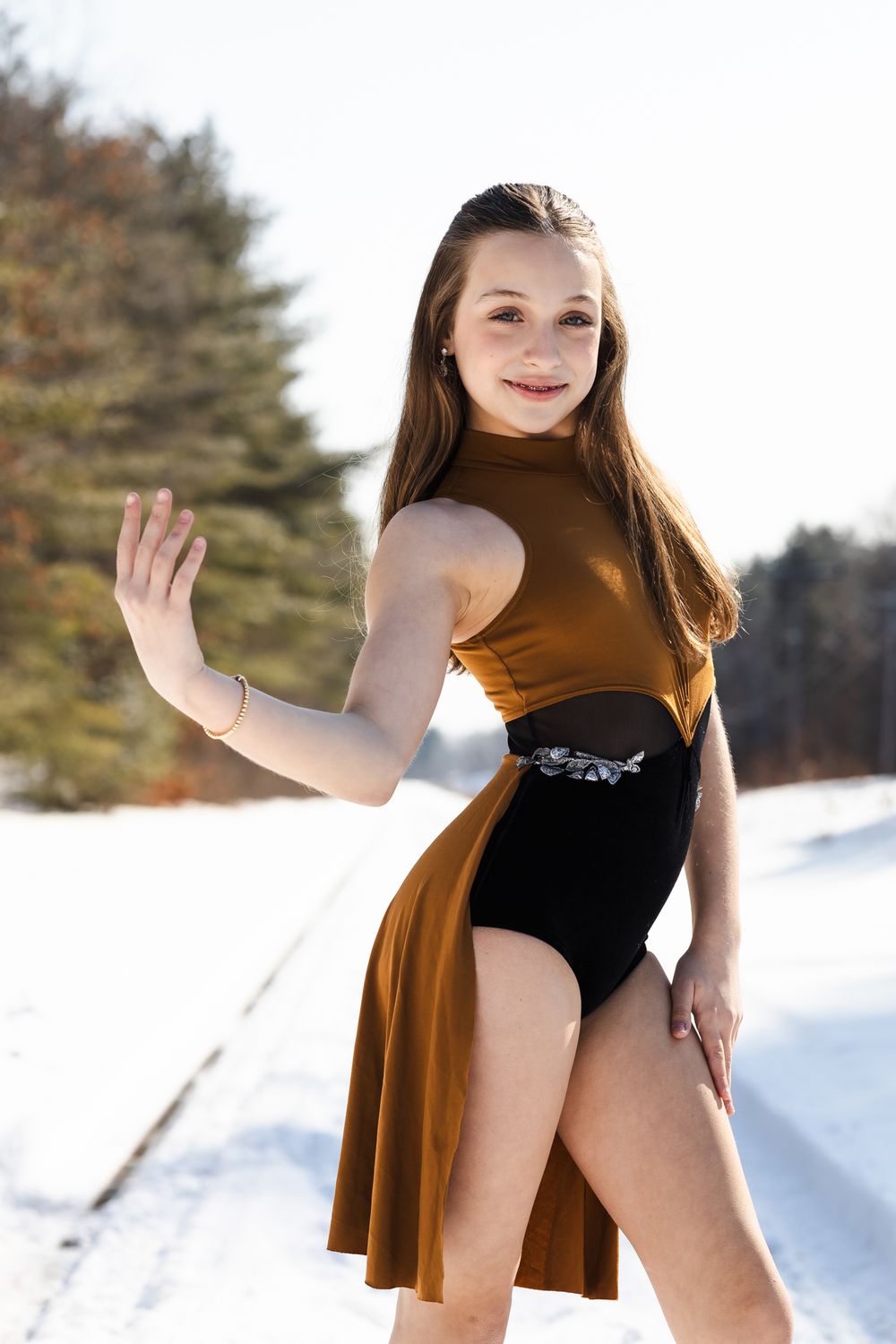 Figure skater in brown costume performs graceful poses against snowy winter backdrop.