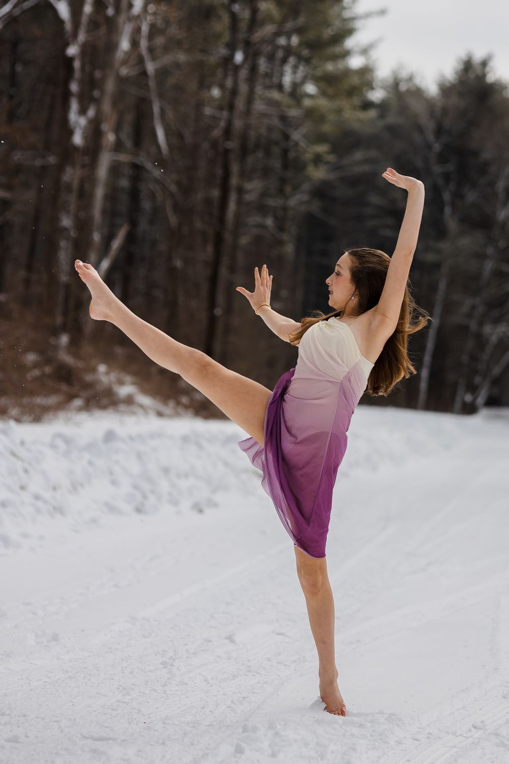 Dancer performs graceful high kick poses in snowy winter forest wearing purple dance attire.