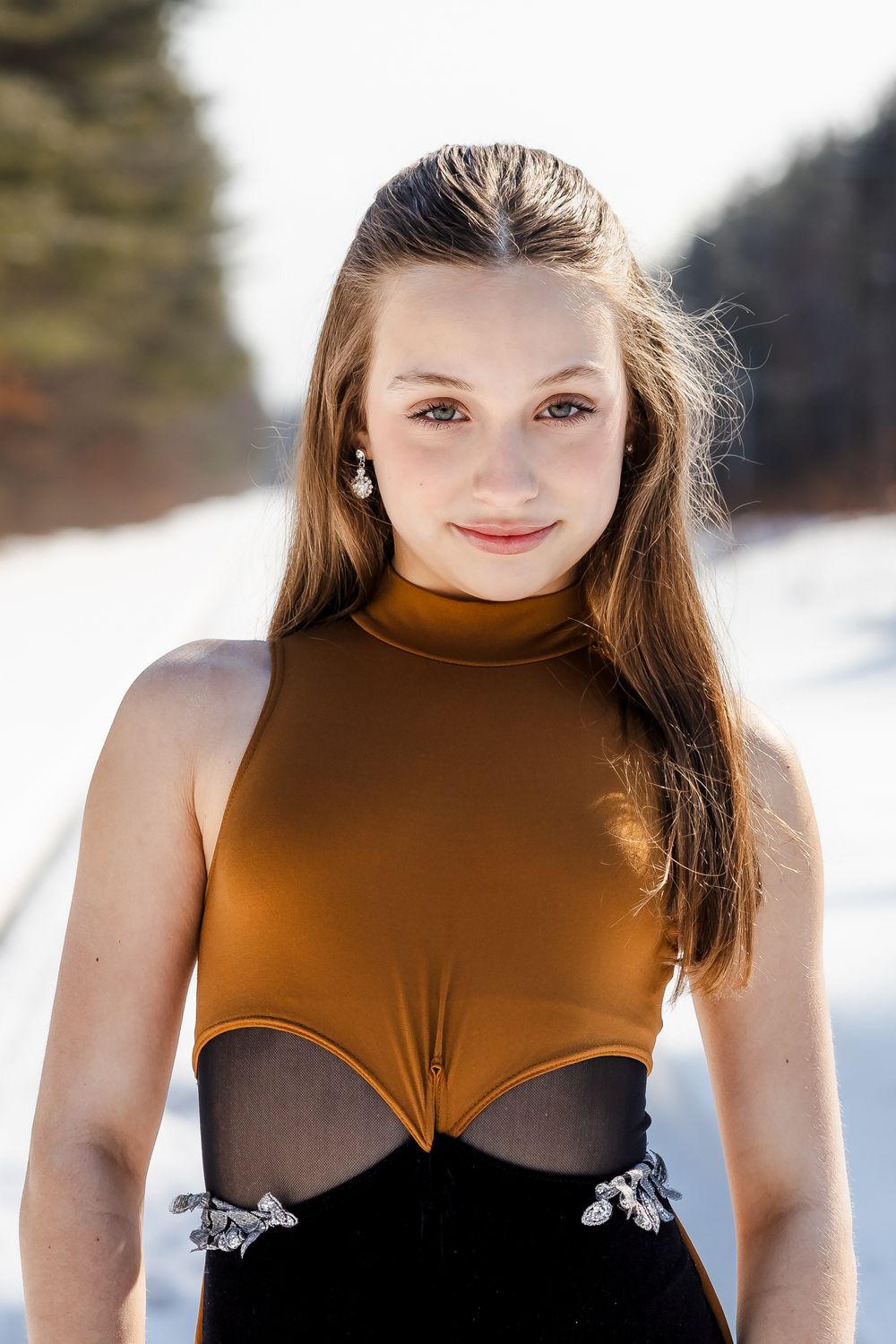 Ice dancer strikes elegant poses in brown and black performance attire on snowy day.