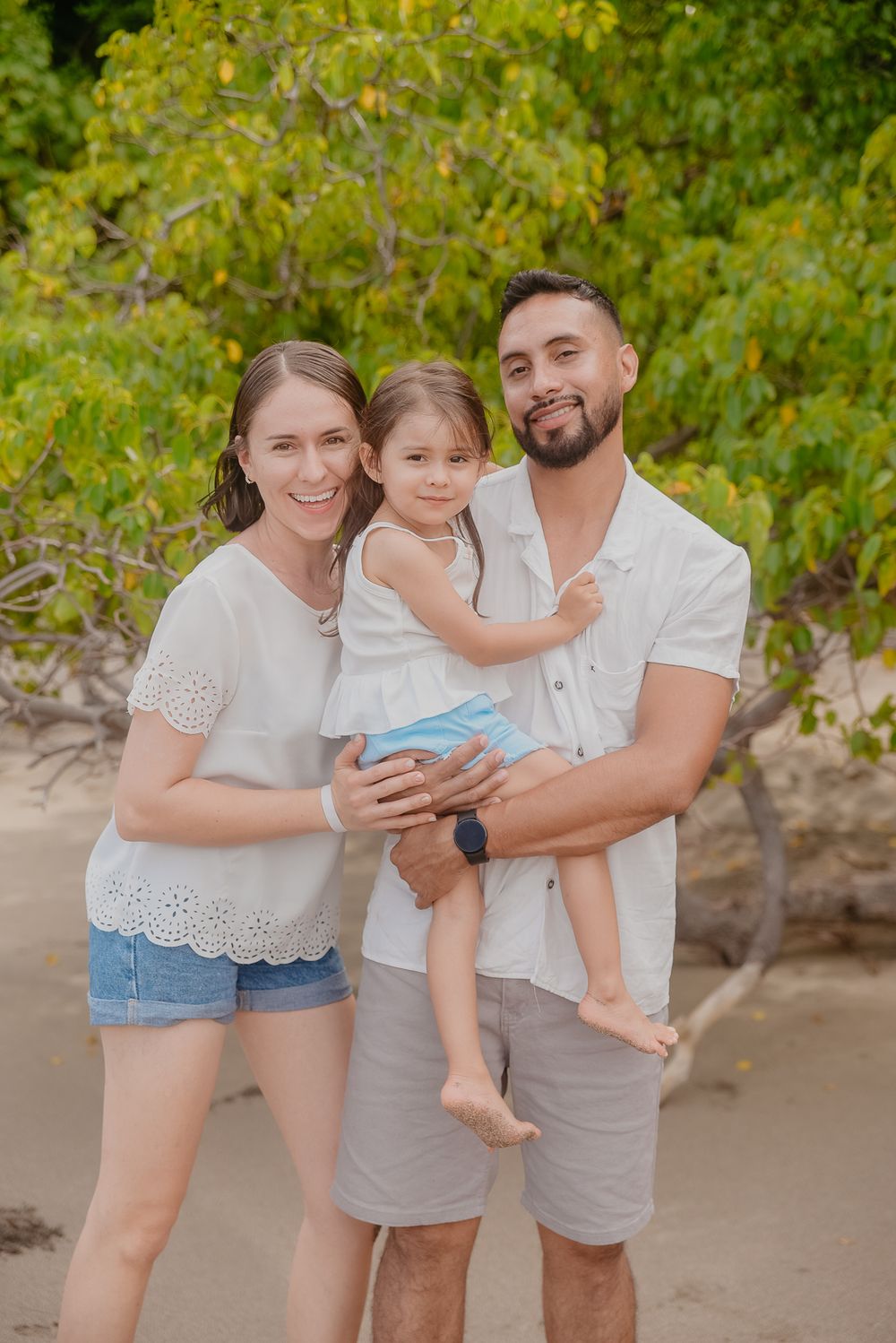 A family in coordinated white and beige outfits poses together for casual beach photos in a natural setting.