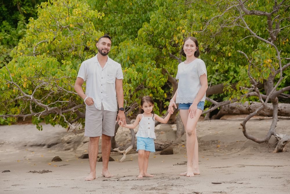 Family walking together on a sandy beach path surrounded by lush green foliage on a sunny day.
