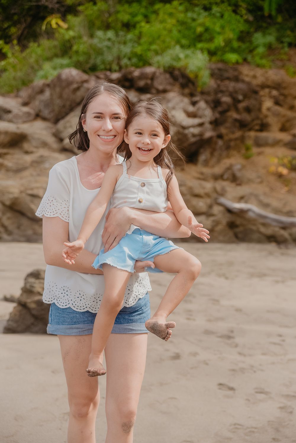 Two people share a joyful moment together on a sandy beach with rocky cliffs in the background.